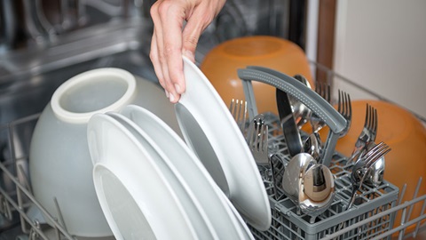 hand steekt een bord in volgeladen afwasmachine